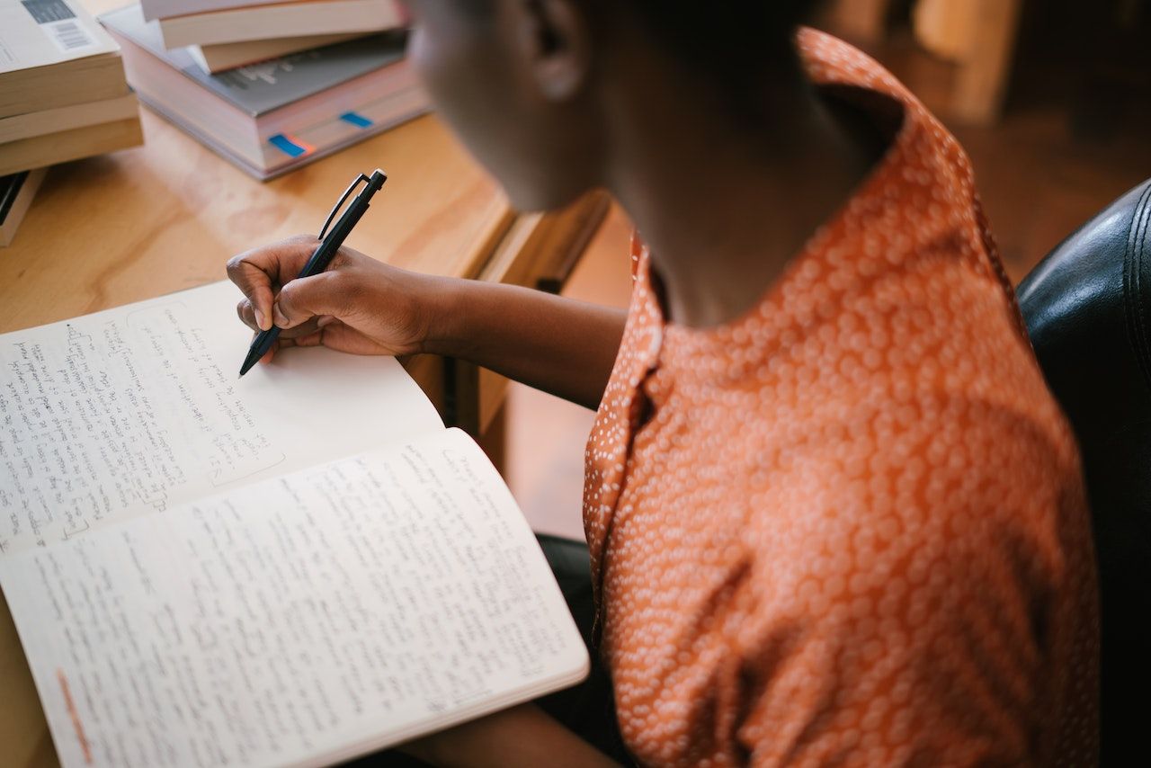 A young Black person writes in a notebook in a humanities course.